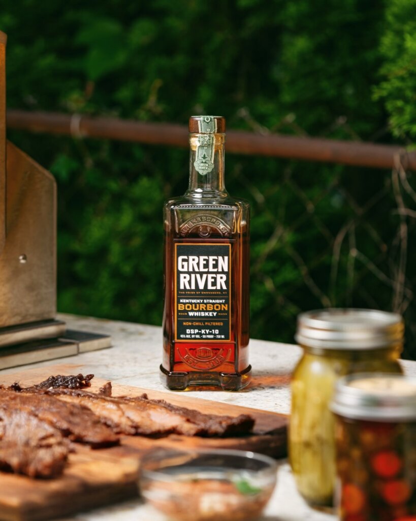 A bottle of Kentucky Straight Bourbon Whiskey from Green River, beside meat charcuterie and pickles.
