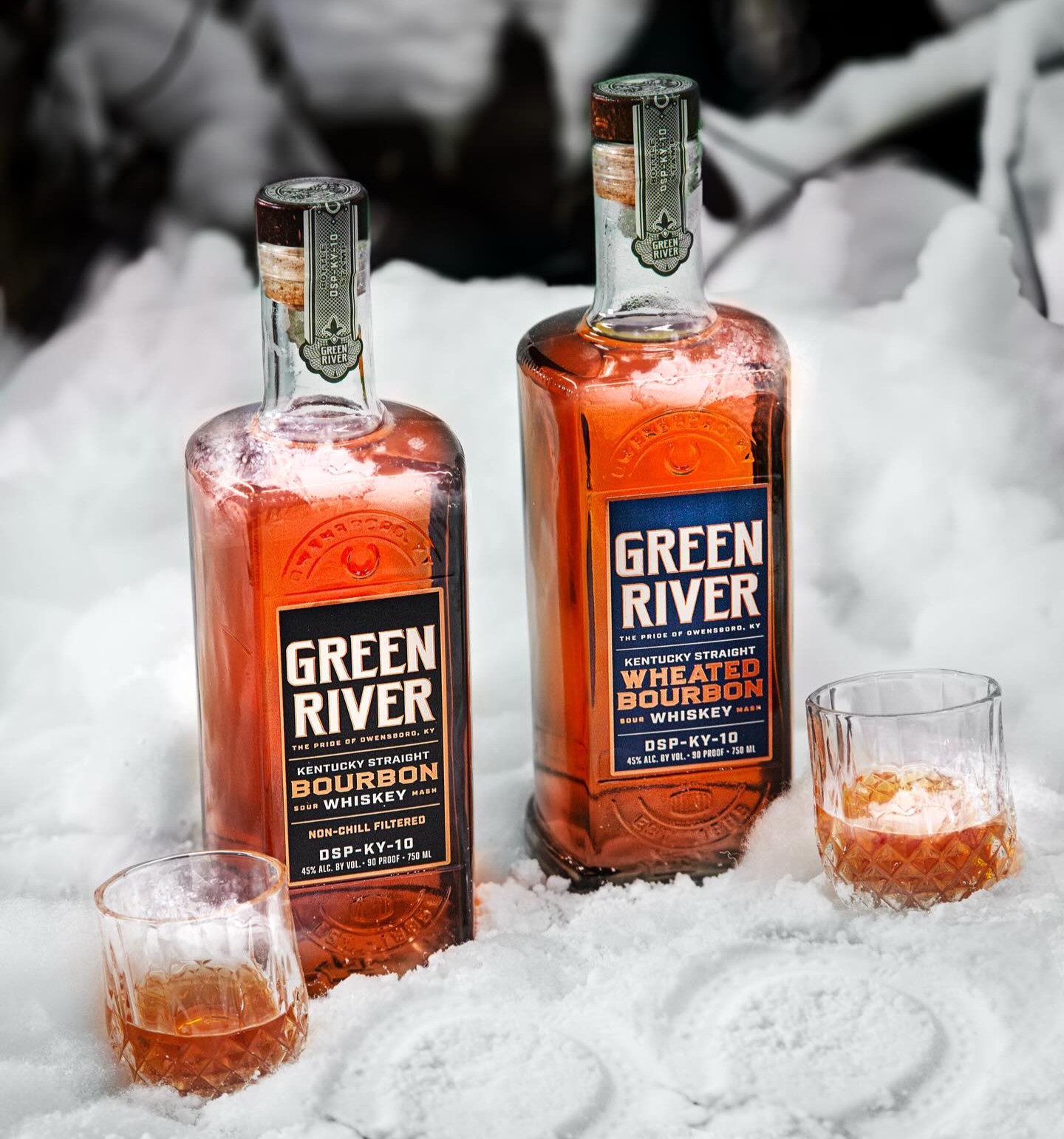 Two bottles of Bourbon Whiskey from Green River Distillery beside two glasses of whiskey on ice.