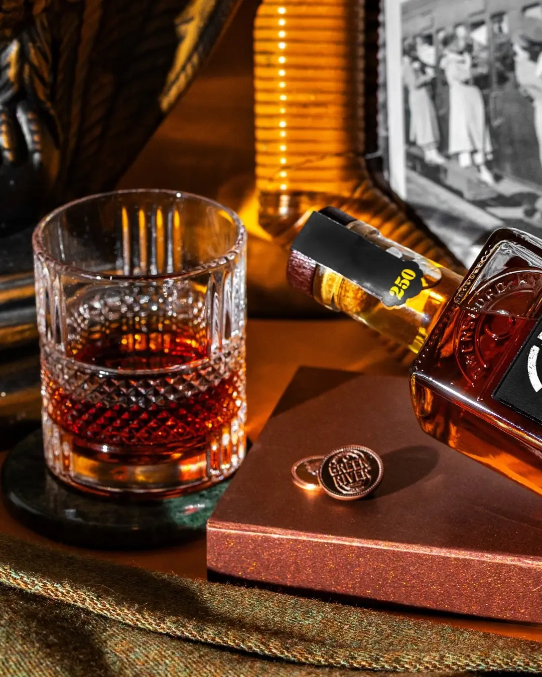 Crystal whiskey glass with amber bourbon beside a Green River bottle in a warm lounge setting.