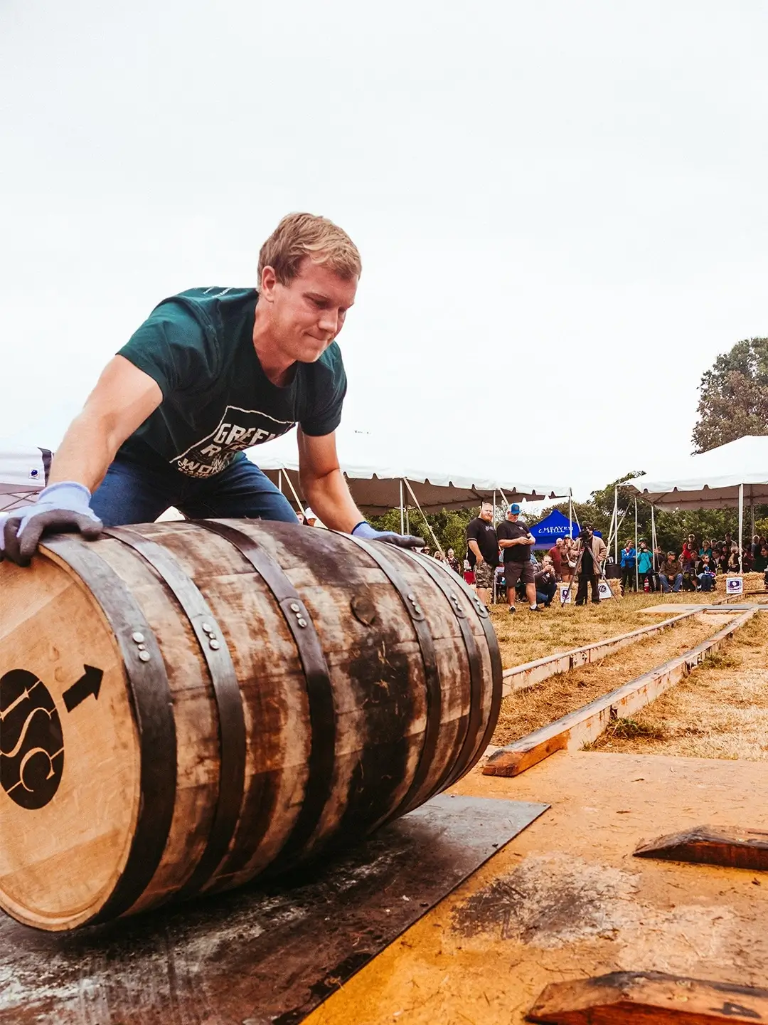 Participant rolling a bourbon barrel at an outdoor Kentucky whiskey festival event.