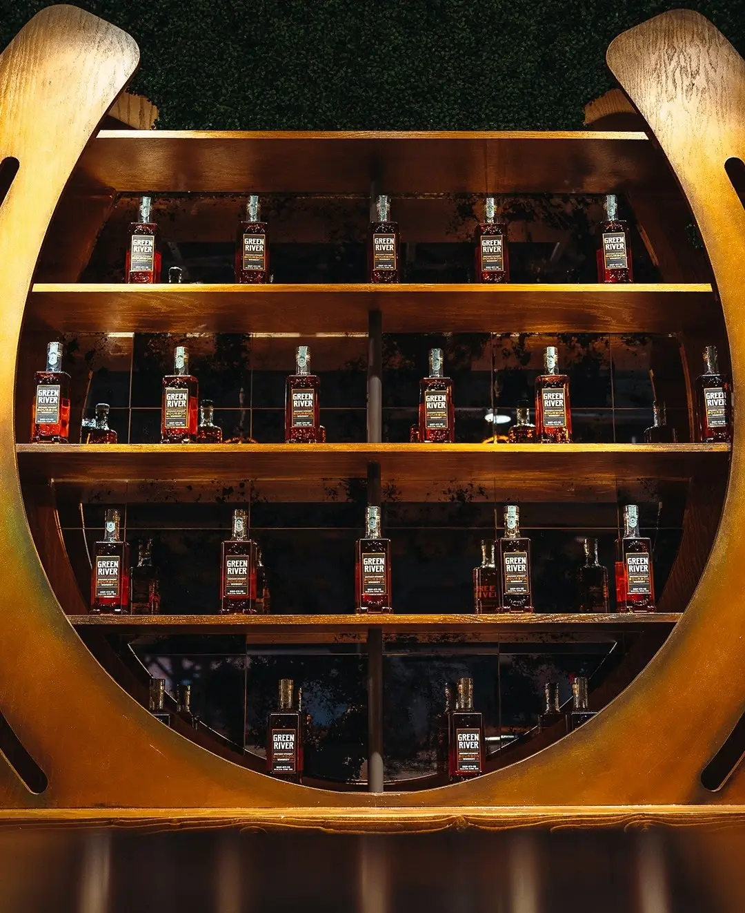 Green River Distillery whiskey bottles displayed on curved illuminated wooden shelves.