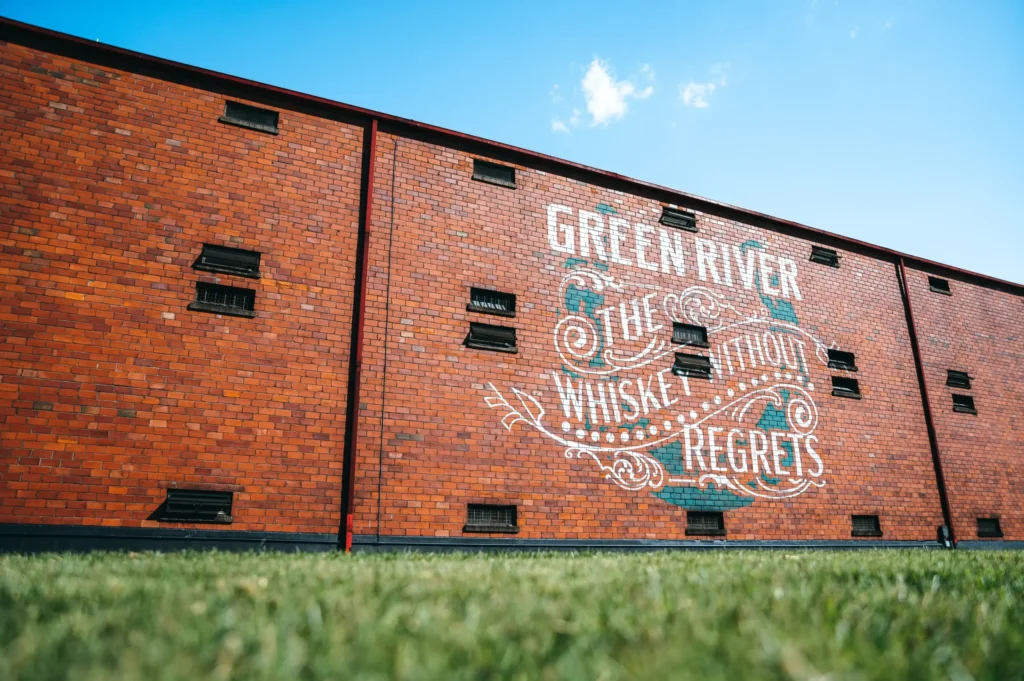Red brick building with white and teal ornamental mural reading Green River Smooth Whiskey Regrets.