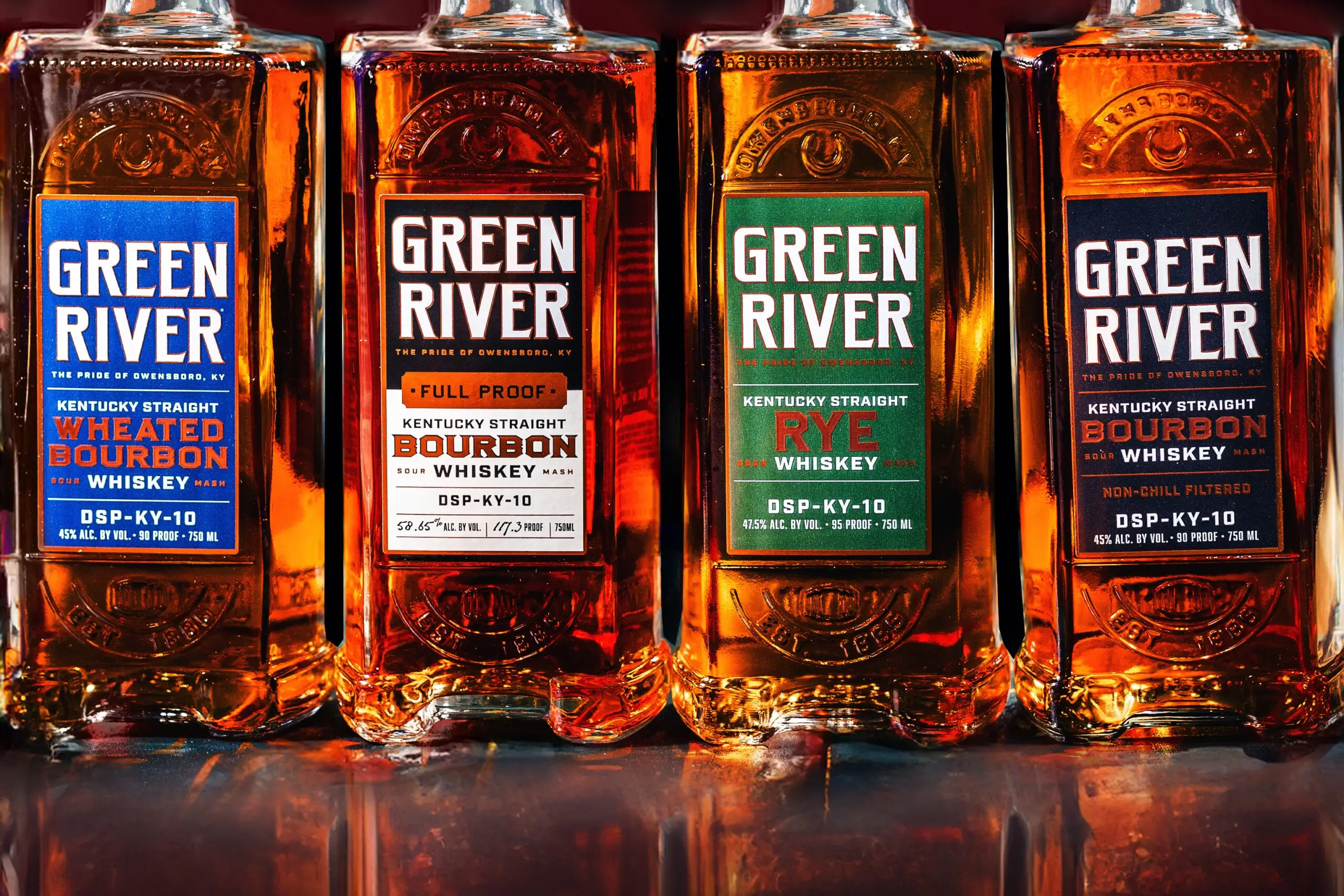 Four Green River Kentucky Straight Bourbon Whiskey bottles with colored labels lined up on a reflective surface.