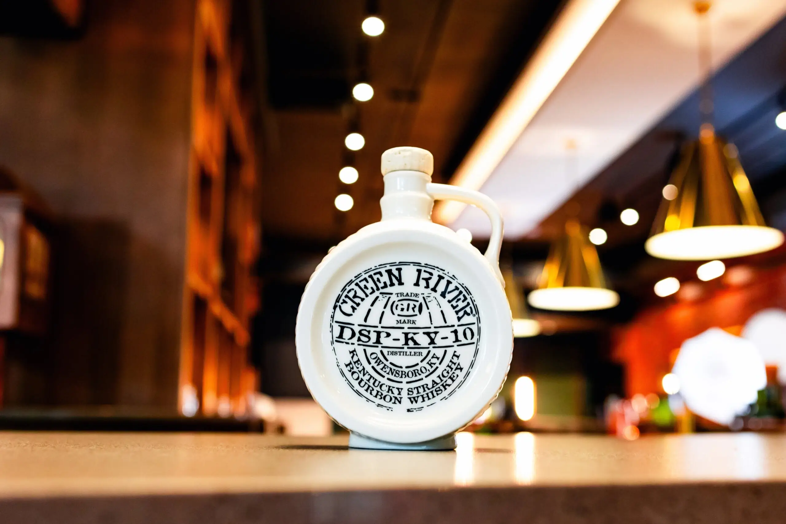 Green River bourbon whiskey ceramic jug on bar counter with warm lighting.
