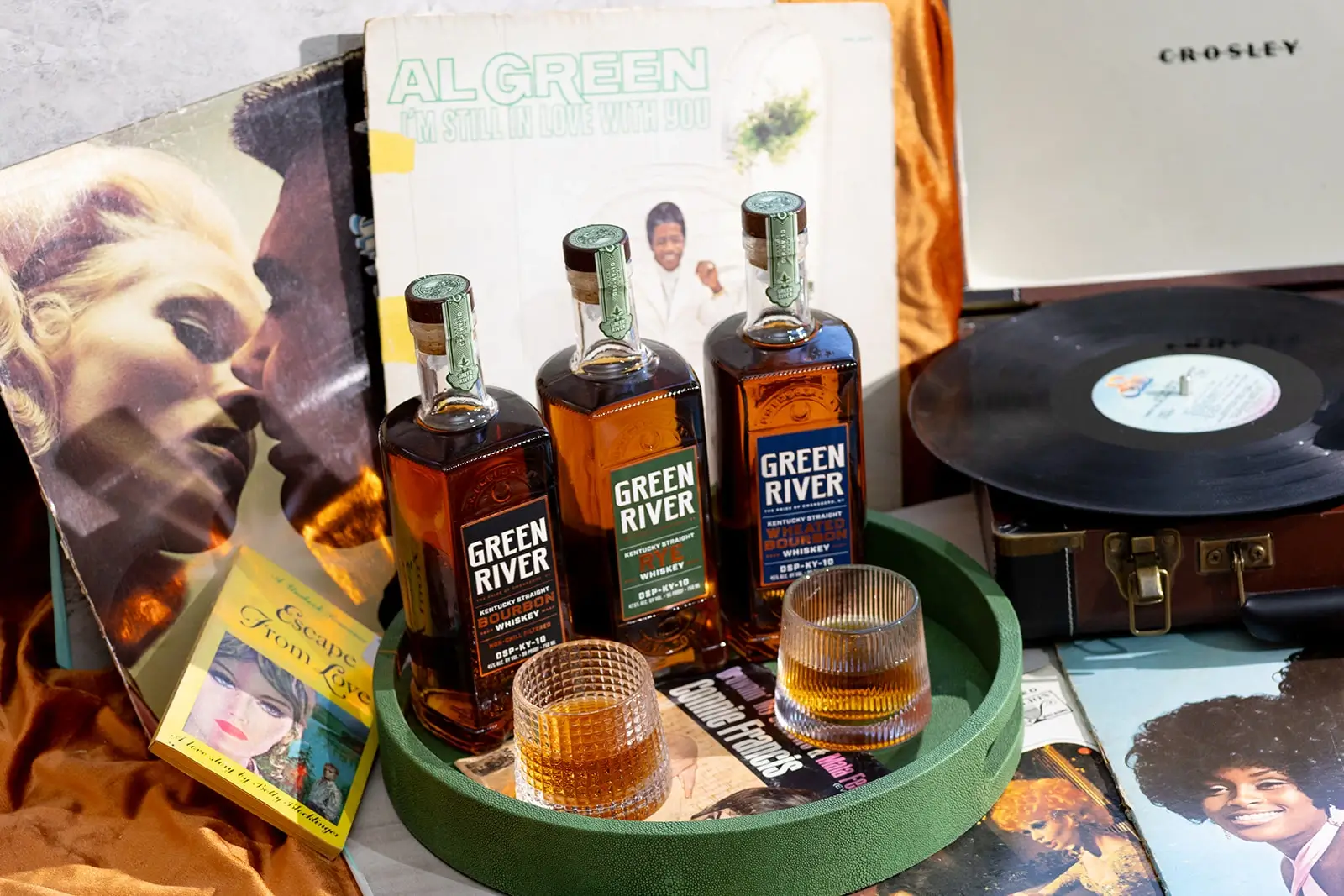 Green River whiskey bottles with glasses on a green tray next to vinyl records and album covers.