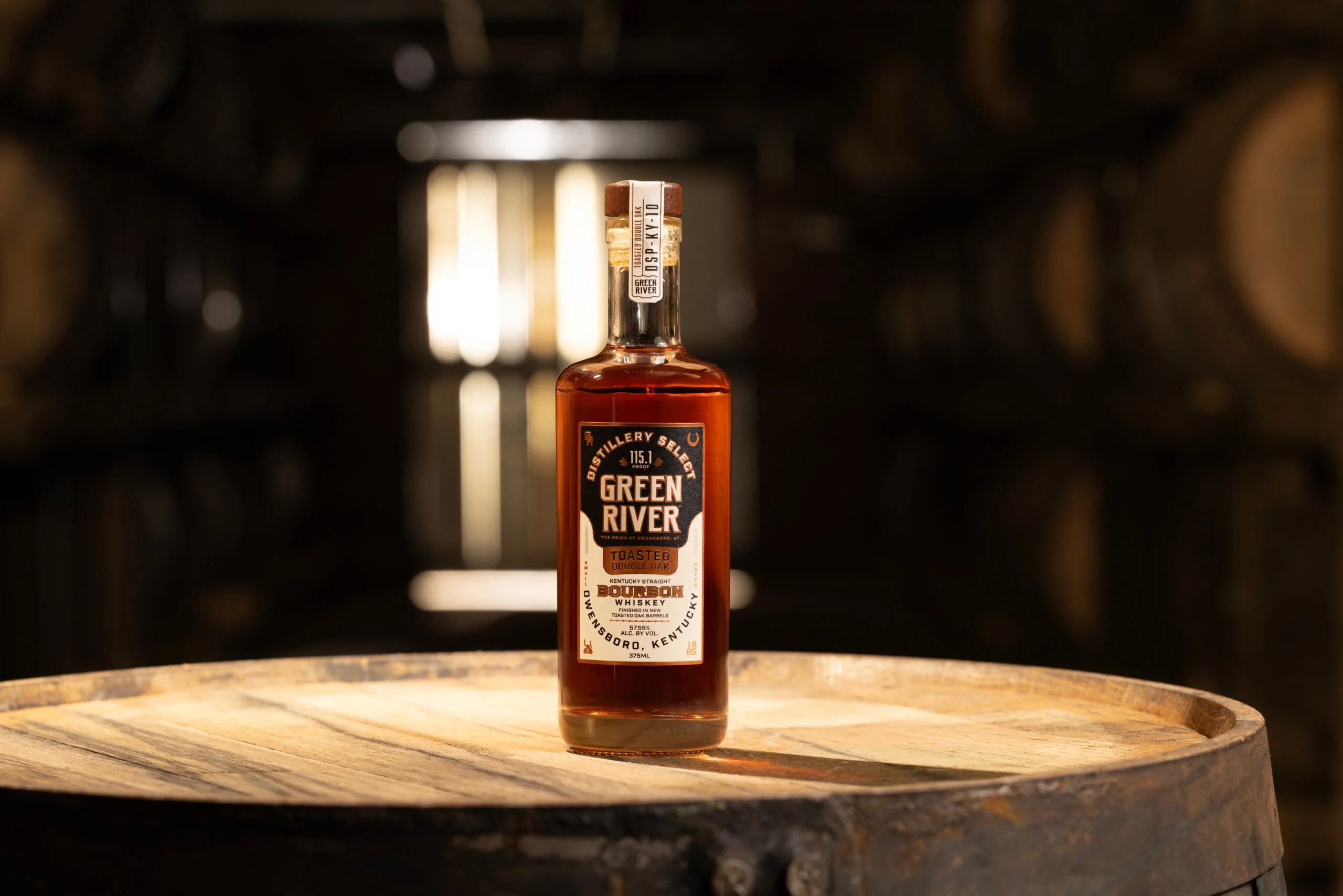Green River bourbon whiskey bottle displayed on a wooden barrel in a distillery setting.